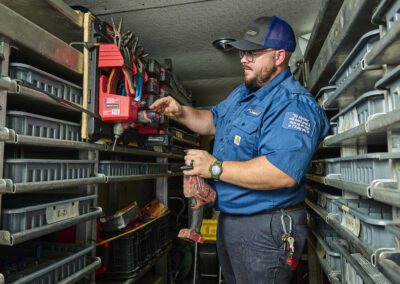 A technician in a blue uniform organizing tools in a van with shelving units